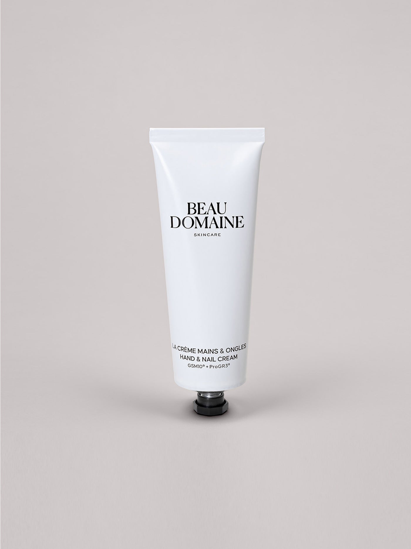 Witte tube Beau Domaine hand- en nagelcrème op een lichtgrijze achtergrond.